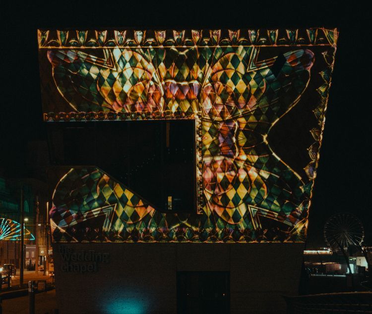 Lighting display of a bejewelled flower overlayed with a diamond pattern projected on the side of a building